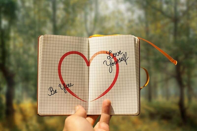 Illustration de la confiance en soi : carnet ouvert avec un cœur et messages positifs, symbolisant l'estime de soi retrouvée grâce à l'hypnose en Loire-Atlantique