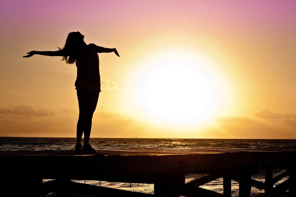 Femme épanouie sur un ponton au coucher de soleil, symbole de liberté retrouvée après une séance d'hypnose pour les phobies.