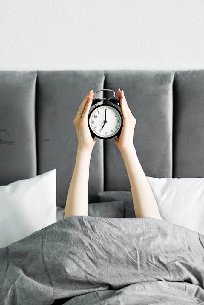 Illustration des troubles du sommeil : mains tenant un réveil dans un lit, représentant l'insomnie traitée par l'hypnose à Saint-Léger-les-Vignes et Nantes Sud.